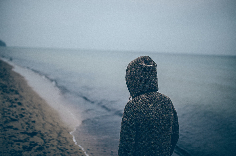 Una persona de espaldas, con una capucha, mirando el mar