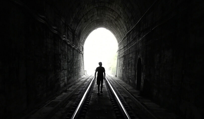 Una persona camina por un tunel oscuro hacia la salida.